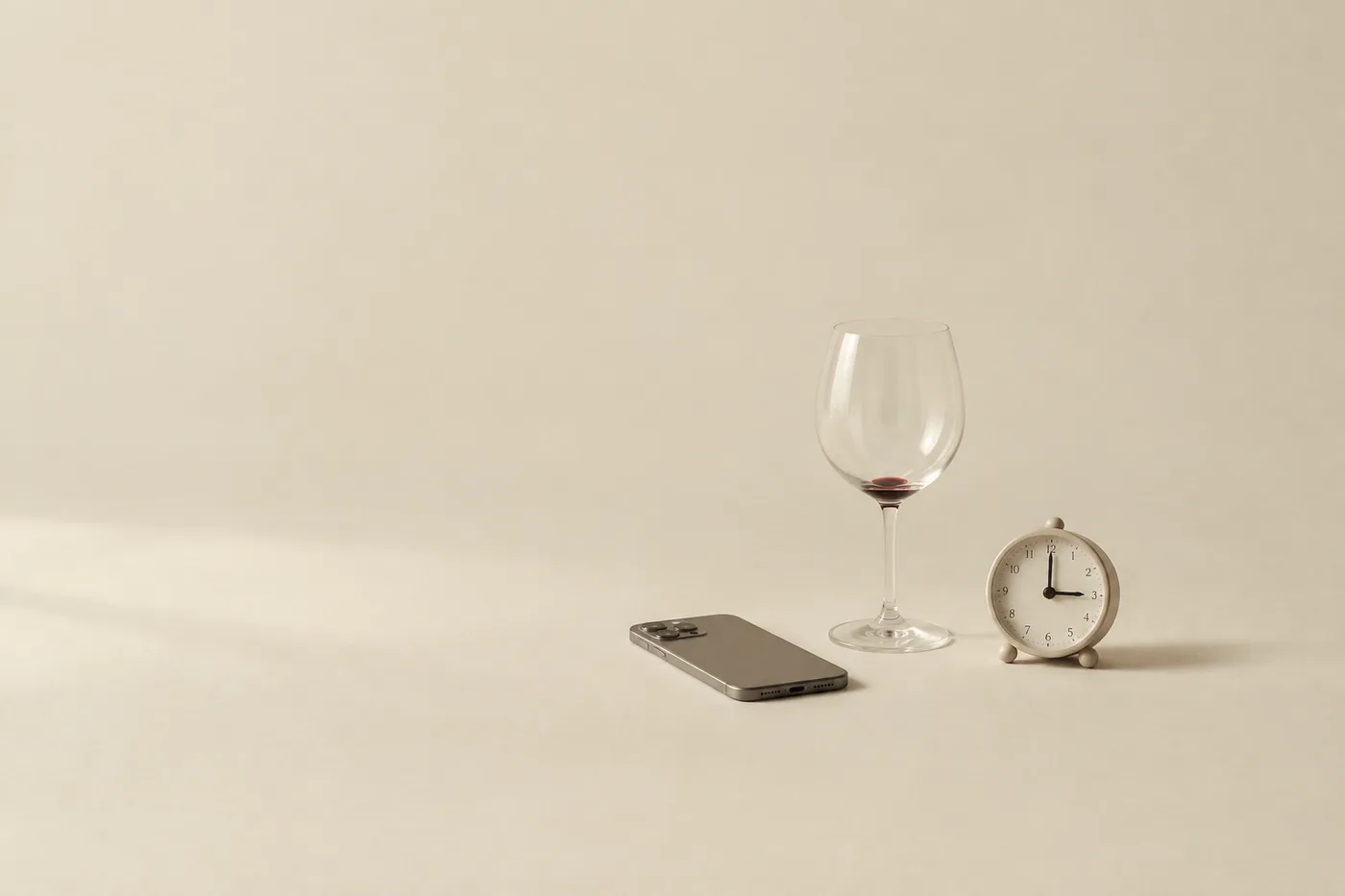 An empty wine glass, a phone face down and a small alarm clock
