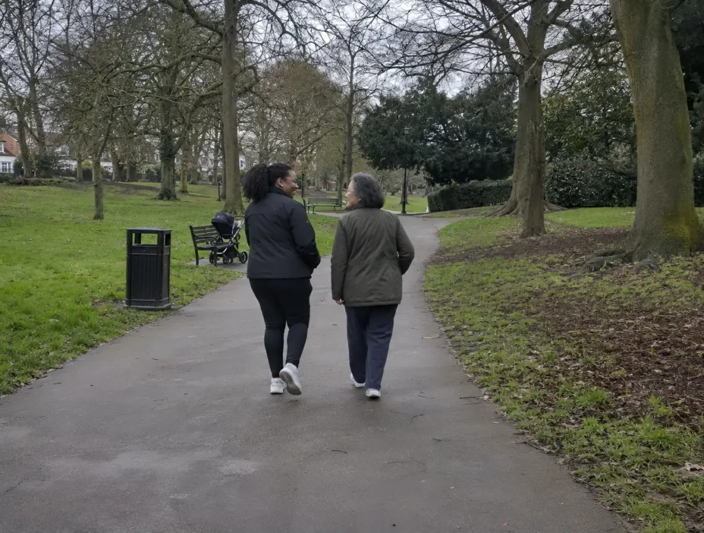 Two women walking and talking on a park path on a cloudy afternoon