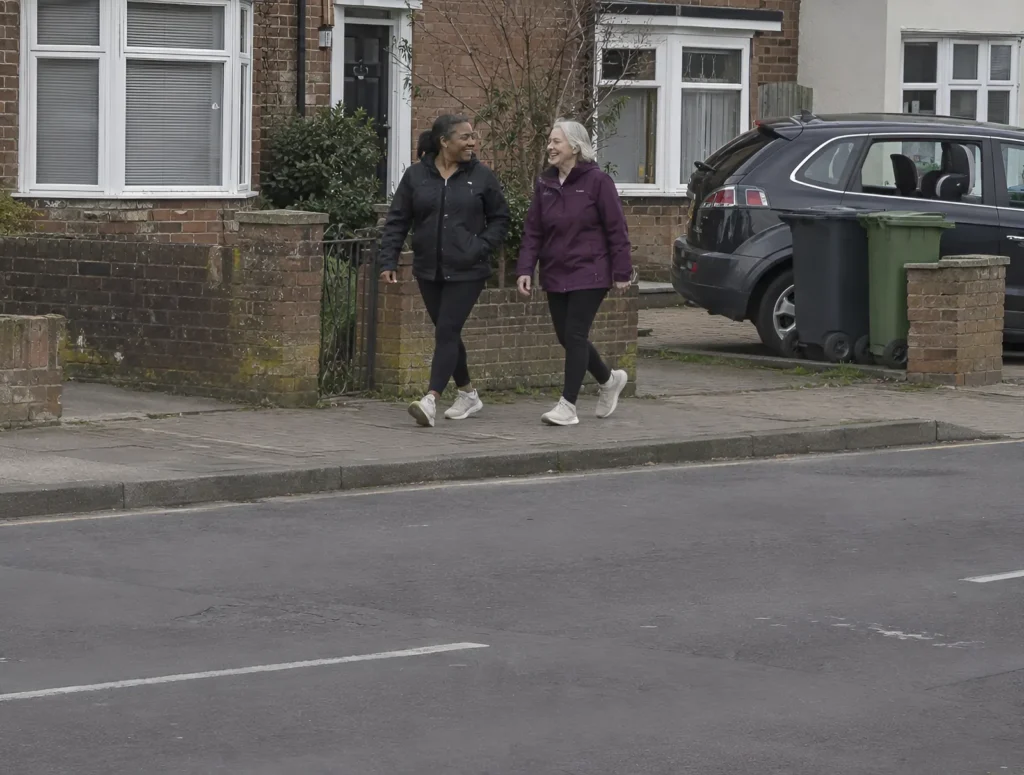 Two women walking fast together on a neighbourhood street on a grey day